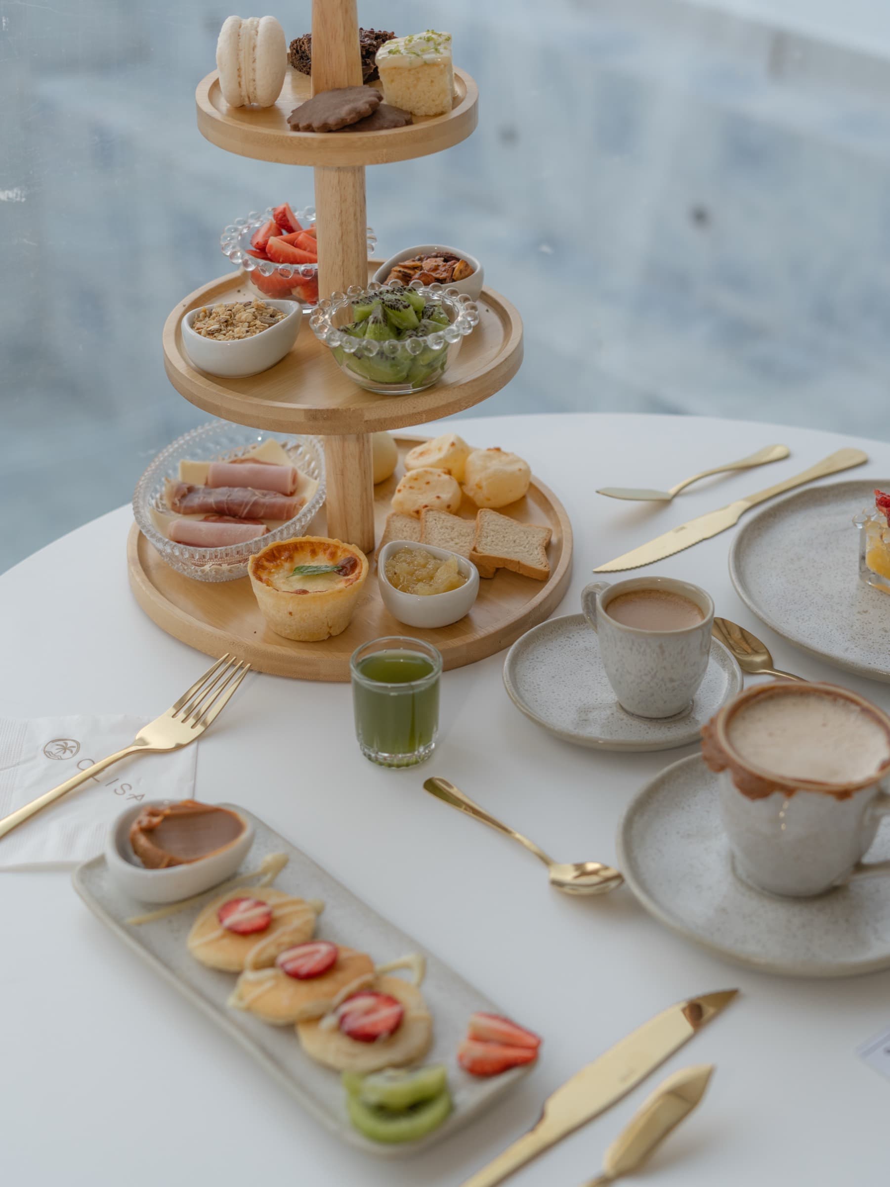 Torre de café da manhã completa, com frutas cortadas, tapioca, iogurte, pães e duas xícaras de café servidas ao lado